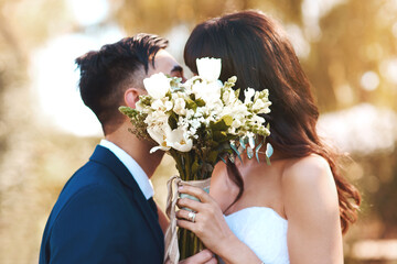 Cover, face and couple with flowers kiss at wedding in celebration of love and marriage. Bride, groom and people show care and support in romantic commitment with floral bouquet outdoor in summer