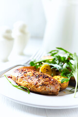 Grilled Chicken Breast with oven baked potatoes and fresh rocket. Bright background. Close up.