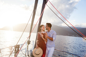 Happy couple in love drinking wine on yacht by sea at sunset. Traveling on sailboat. Travelers have...