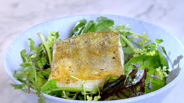 Close-up of man's hand squeezing lime juice on white fish, pike-perch zander and salad. 4k Slow motion 100fps video.