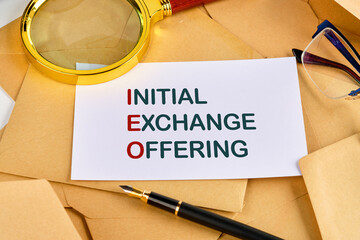 Business concept IEO INITIAL EXCHANGE OFFERING on a blank sheet near a pen, magnifying glass and...