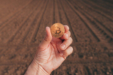 Farmer holding bitcoin cryptocurrency coin in plowed field, financial investment in agricultural...