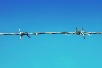 Sharp barbed wire against blue sky, containment and imprisonment concept