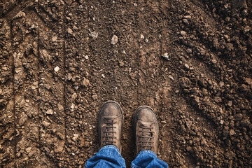 Top view of farmer's feet in boots standing on countryside dirt road
