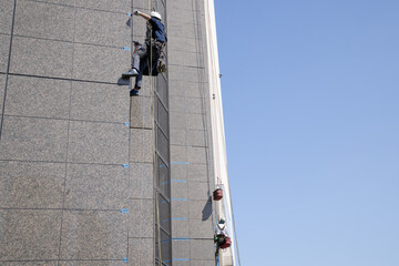 ロープにぶら下がりビルの外壁の補修をする作業員