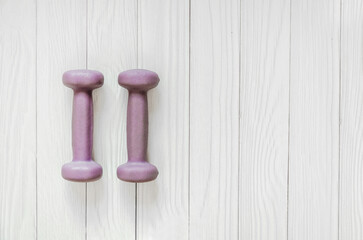 two lilac dumbbells lie on a white wooden background. horizontal banner, space for text
