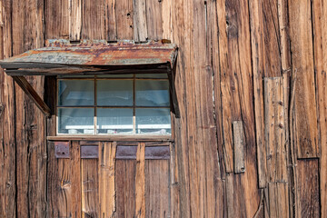 Window with a metal awning on the wall of an abandoned wooden shack