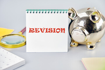 Revision inscription on a vertically standing notebook near a piggy bank, a magnifying glass and a...