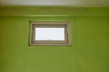 green cracked wall with small glass window to allow natural light to enter room or hallway,...