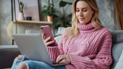 Young woman with pink sweater using a mobile phone and laptop at home