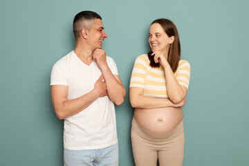 Smiling delighted young married pregnant family standing isolated over light green background man...
