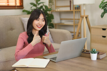 Young businesswoman showing thumbs up gesture and talking with partners while meeting in video call