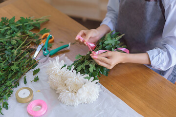 Floristry concept, Woman florist making white chrysanthemum bouquet and tie ribbon at flower shop