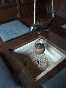 Boiling the old teapot on hot glowing coals in japanese traditional irori hearth with wooden carved Jizai kagi koi carp fish figure 