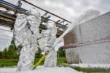 Firefighters in special heat protective suits use foam to extinguish a tank of highly flammable...