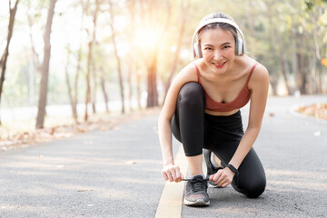 Young fitness woman with headphone tie shoelaces on road  before running.