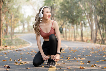 Young fitness woman with headphone tie shoelaces on road  before running.