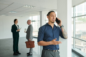 Businessman taking on phone when coworkers having small talk in background