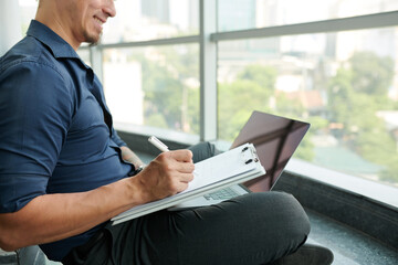 Smiling businessman taking notes for designer when watching product presentation on laptop