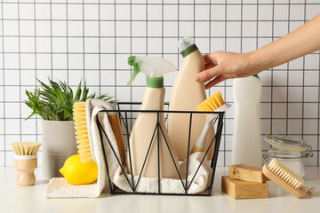 Basket with towel and bottles of detergents, hand, brushes and plant on light background