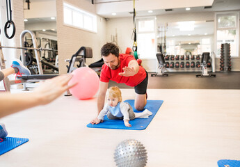 Father smiling at baby while performing exercise above. Group exercise class, fitness or pilates...