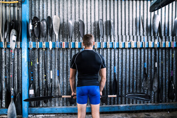 Rear view of young canoeist standing in front of wall with paddles. Concept of canoeing as dynamic...