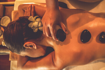 Closeup hot stone massage at spa salon in luxury resort with warm candle light, blissful woman...
