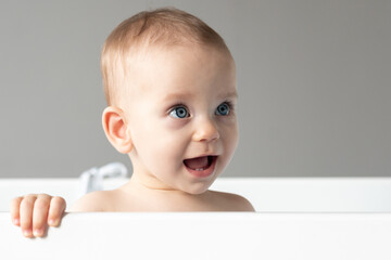 Close-up of the face of a baby laughing out loud and looking out of a crib with interest