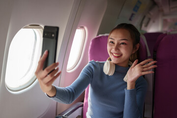 Asian female tourist checks notifications on smartphone while seated on airplane A businesswoman happily shares media from her phone, taking photos of the view from the window during a flight.