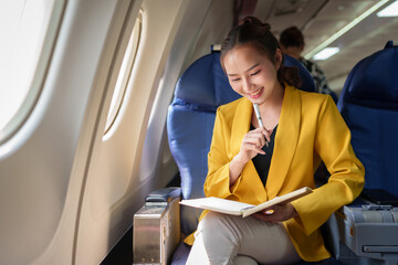 Beautiful successful Asian businesswoman sitting in a plane and working on a notebook. Notes,...