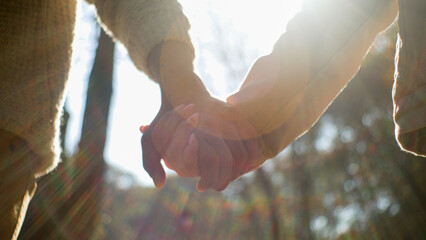 Close-up unrecognizable couple in love man woman holding hands in sunlight walking in park outdoors...