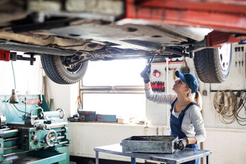 Female auto mechanic elevating car on car lift, changing oil. Beautiful woman working in a garage,...