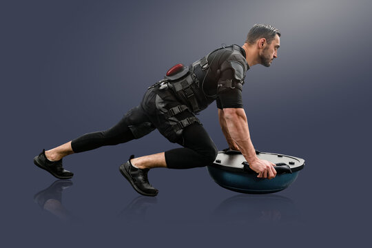 Strong man in EMS suit doing exercise on bosu ball, Exercise technology: Male with electro stimulator in studio backdrop, great for fitness magazines