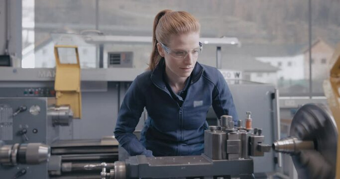 Focused craftswoman working metal on the lathe with precision