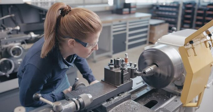 Focused craftswoman working metal on the lathe talking with colleague