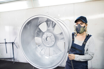 Female car painter, paingting vehicles in auto body shop. Young woman holding spray gun, spraying...