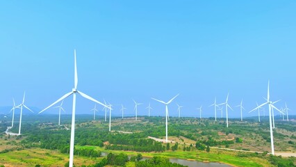 A tranquil wind farm adorns the horizon, turbines swaying elegantly under a serene sky. This aerial...