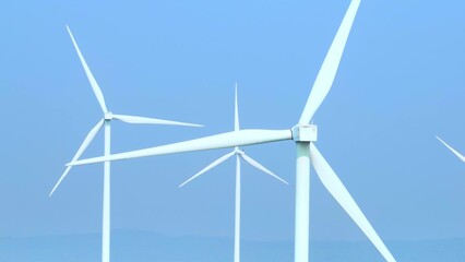 Aerial perspective reveals towering wind turbines against a serene sky, their rotating blades...