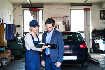 Female auto mechanic talking with customer, explaining repair, problem. Scheduling date of annual...