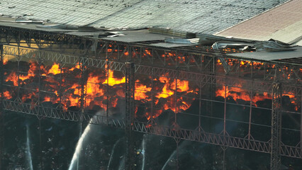 A raging inferno consumes an industrial site, its destructive flames dancing amidst collapsed...