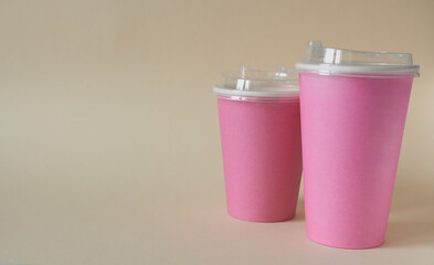 Two pink paper coffee or tea cups on a beige background.