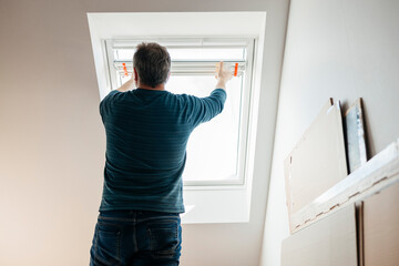 Man installing blinds on attic window at home