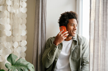 Smiling man talking on mobile phone sitting by hanging decor at home