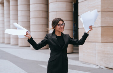 Dynamic professional woman, joyfully multitasking with documents outdoors, showcasing efficiency...