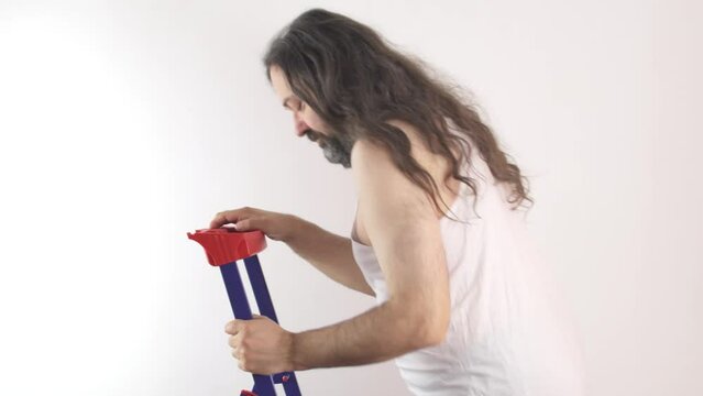 A poor man goes up and down a folding metal ladder. A man with a dissatisfied grimace. A man in a cheap, white, wrinkled undershirt. Bankrupt man without a job. 