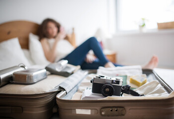 Beautiful woman lying on bed next to packed suitcase. Solo traveller preparing for trip.