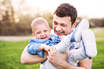 Fototapeta premium Father holding little toddler boy playing, having fun during warm spring day. Father's day concept.