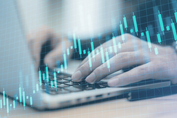 Close up of male hands using laptop on desk with creative growing candlestick forex chart on blue...