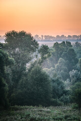 Red sunrise over the field with trees and forest . Morning at summer . Fog over the field and trees . Beautiful landsapes . Red sky and blue hour on nature . Smoothly foggy morning 