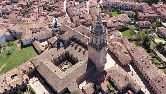 Drone view of Spanish town of El Burgo de Osma in spring overlooking traditional terracotta tiled roofs of residential buildings surrounded by green hills and medieval Roman Catholic gothic cathedral